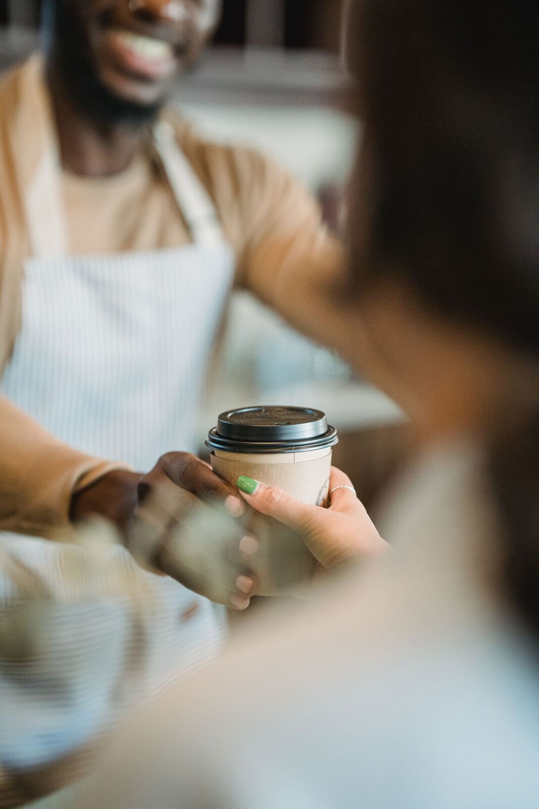 Manos entregando un vaso de café por encima del mostrador