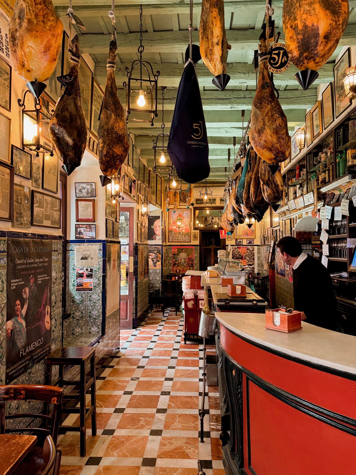Interior de un bar tradicional con jamones colgados y clientes en la barra